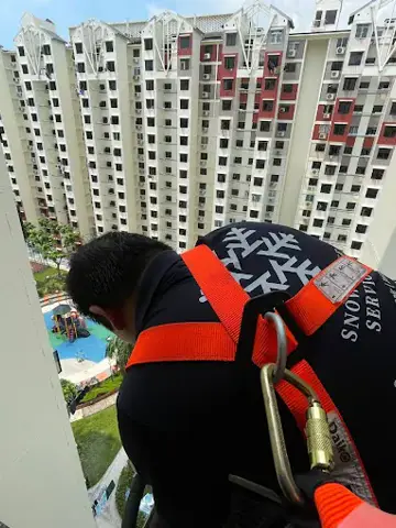 Technician in a safety harness at an outdoor unit on an HDB block